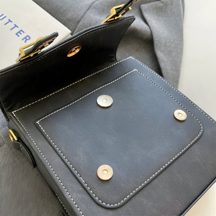 Gros plan d'un sac en cuir noir ouvert avec coutures blanches, fermoirs magnétiques et boucle dorée., 46193901863136,46193901895904,46193901928672