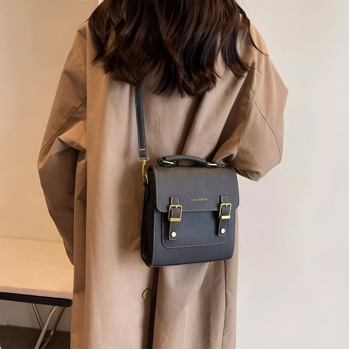 Personne vue de dos avec un sac cartable noir à boucles dorées et coutures blanches., 46193901863136,46193901895904,46193901928672