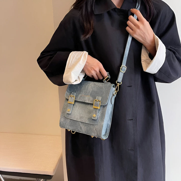 Personne en manteau noir avec poignets blancs, tenant un sac bandoulière bleu gris à boucles dorées., 46193901863136,46193901895904,46193901928672