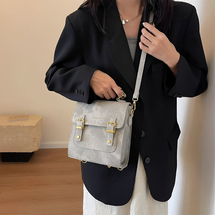 Femme en blazer noir tenant un sac à main gris avec bandoulière et détails dorés., 46193901863136,46193901895904,46193901928672