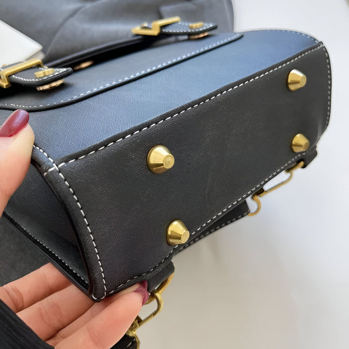 Main tenant un sac noir texturé avec coutures blanches et clous dorés sur le dessous., 46193901863136,46193901895904,46193901928672