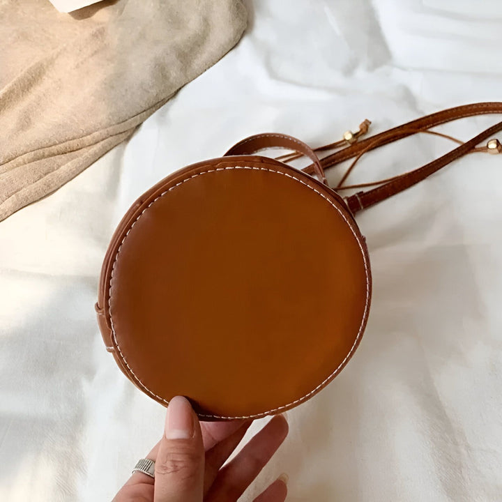 Sac rond en cuir marron avec surpiqûres blanches tenu par une main., 46194011308256,46194011373792
