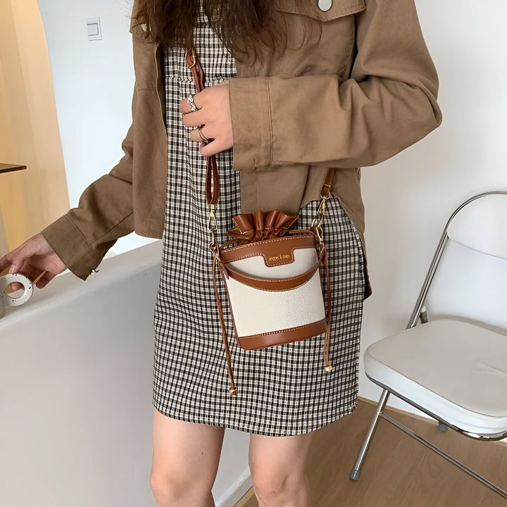 Femme en robe à carreaux et veste marron, portant un petit sac seau blanc et marron., 46194011308256,46194011373792