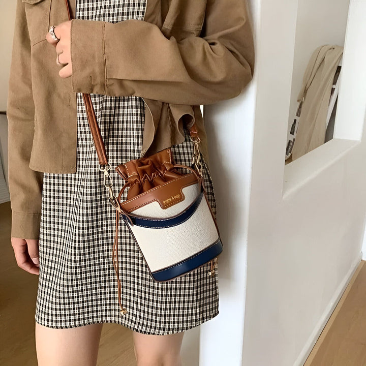 Femme portant un sac seau marron, blanc et bleu avec une robe à carreaux et une veste., 46194011308256,46194011373792