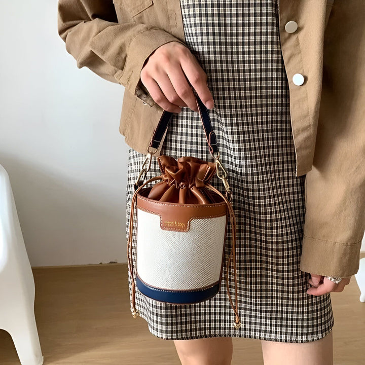 Sac seau blanc, marron et bleu marine porté par une personne en robe à carreaux et veste beige., 46194011308256,46194011373792