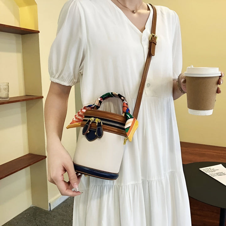 Sac à main cylindrique blanc et marron orné d'un foulard coloré, porté par une femme., 46194010128608