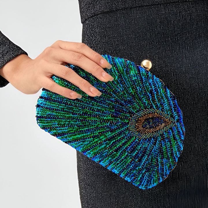 Main tenant une pochette de soirée bleue et verte ornée de sequins et perles motif plume de paon., 46193930830048,46193930862816,46193930895584