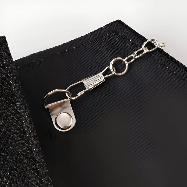 Détail d'un fermoir métallique avec chaîne sur un tissu noir., 46194029002976,46194029035744,46194029068512,46194029101280,46194029134048