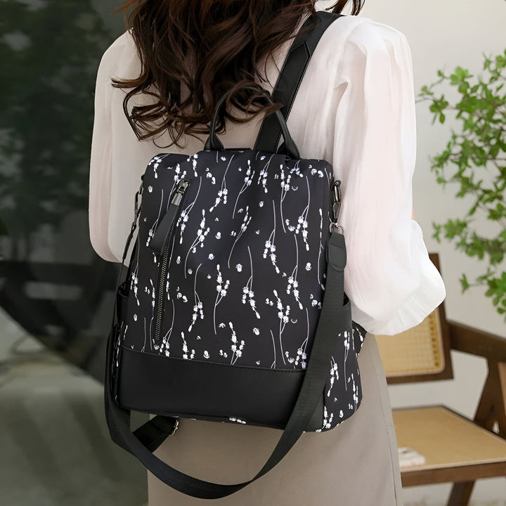Sac à dos noir à motif floral blanc avec bandoulière, porté par une femme., 46193997971680,46193998004448,46193998037216,46193998069984