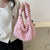 Un sac à main rose texturé avec des poignées en forme de boucle porté par une femme.