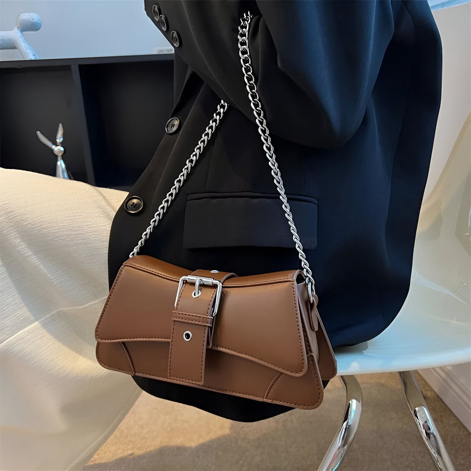 Un sac à main brun avec une chaîne argentée portée par une femme portant un blazer noir.