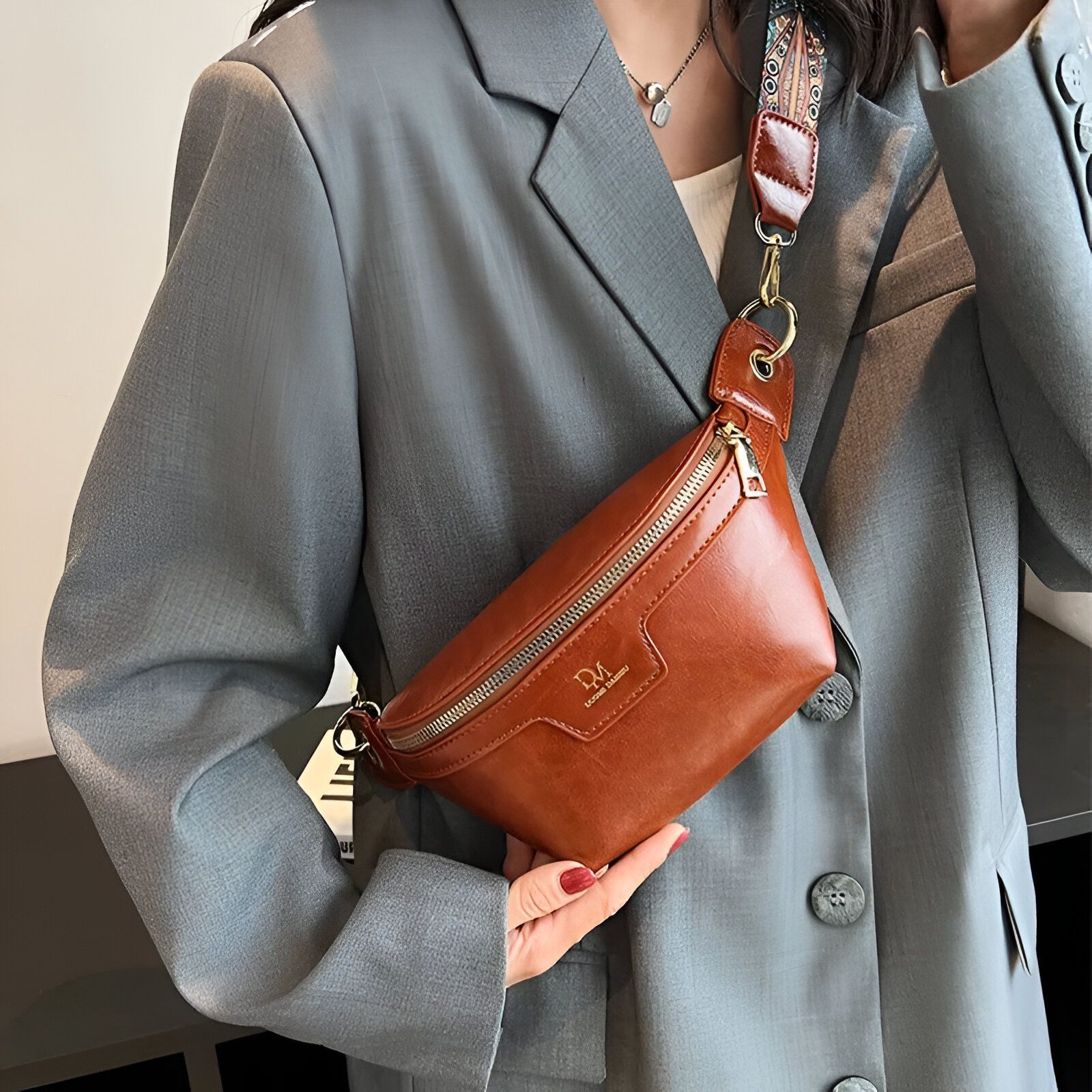 Une femme porte un sac banane marron en cuir avec une sangle en tissu à imprimé coloré.