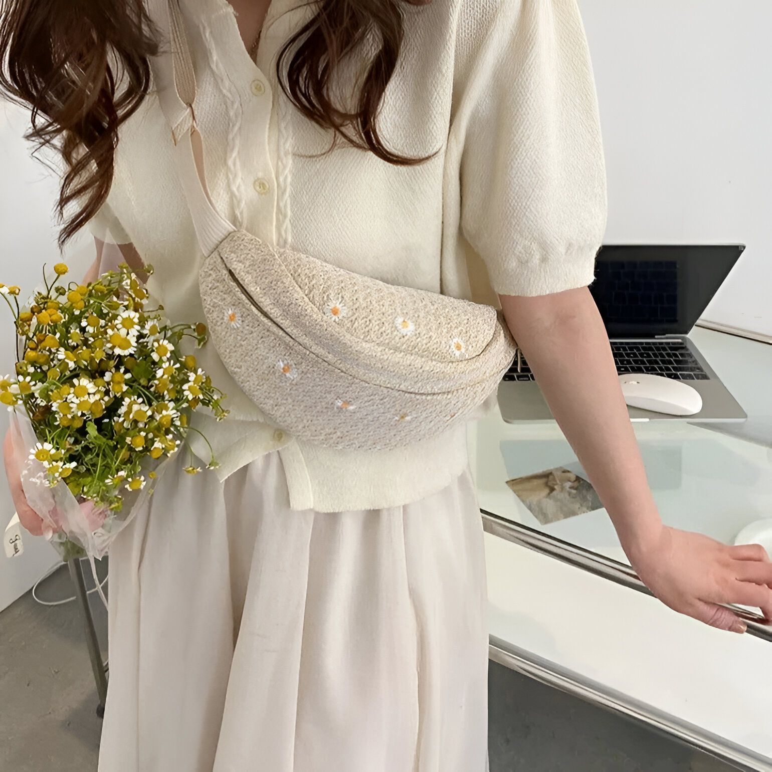 Une femme portant une jupe blanche et un chandail crème avec une ceinture banane en tissu beige brodée de marguerites.