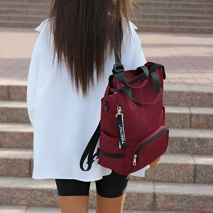 Femme de dos portant un sac à dos bordeaux Tigernu avec lanières noires, vêtue d'une chemise blanche et short., 46193876205792,46193876238560,46193876271328
