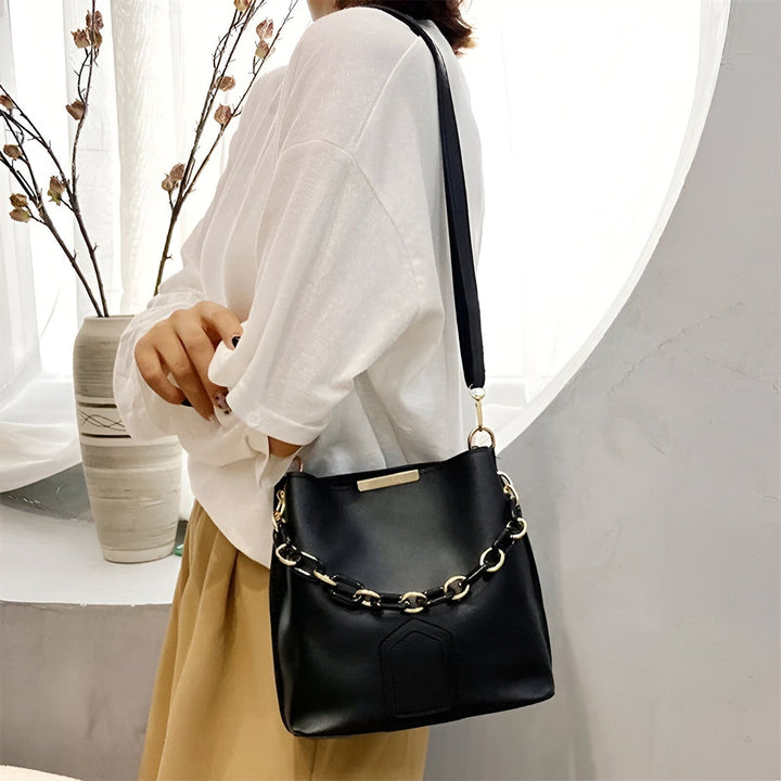 Personne portant un sac à bandoulière noir orné d'une chaîne dorée., 46193874272480,46193874305248,46193874338016,46193874370784,46193874403552,46193874436320