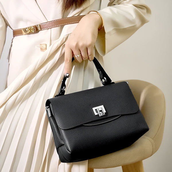 Sac à main noir en cuir grainé avec fermoir argenté, tenu par une femme en robe beige plissée., 46193863557344