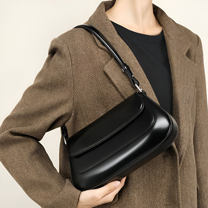 Sac à bandoulière en cuir noir porté par une personne en veste marron à chevrons., 46193864507616