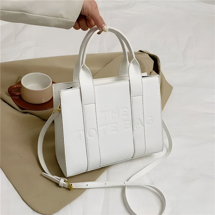 Sac cabas blanc avec bandoulière et poignées, texte embossé "THE TOTE BAG"., 46193877811424,46193877844192,46193877876960,46193877909728,46193877942496,46193877975264,46193878008032,46193878040800