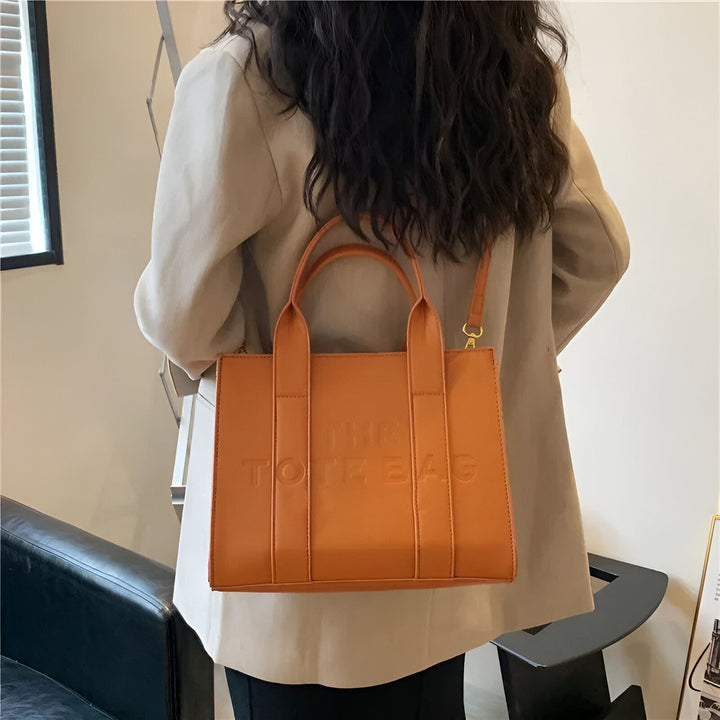 Personne de dos portant un sac tote bag orange avec le texte "THE TOTE BAG" gravé., 46193877811424,46193877844192,46193877876960,46193877909728,46193877942496,46193877975264,46193878008032,46193878040800