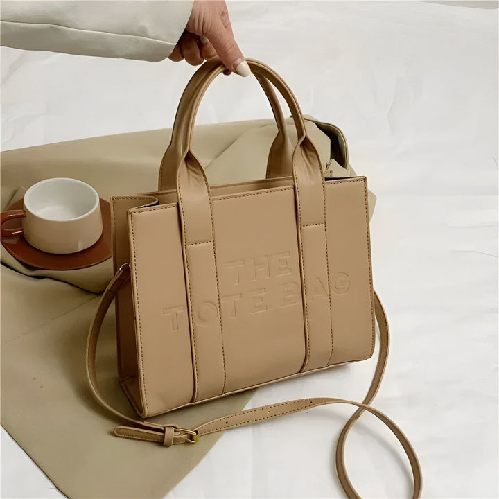 Main tenant un sac tote bag beige avec inscription "THE TOTE BAG"., 46193877811424,46193877844192,46193877876960,46193877909728,46193877942496,46193877975264,46193878008032,46193878040800