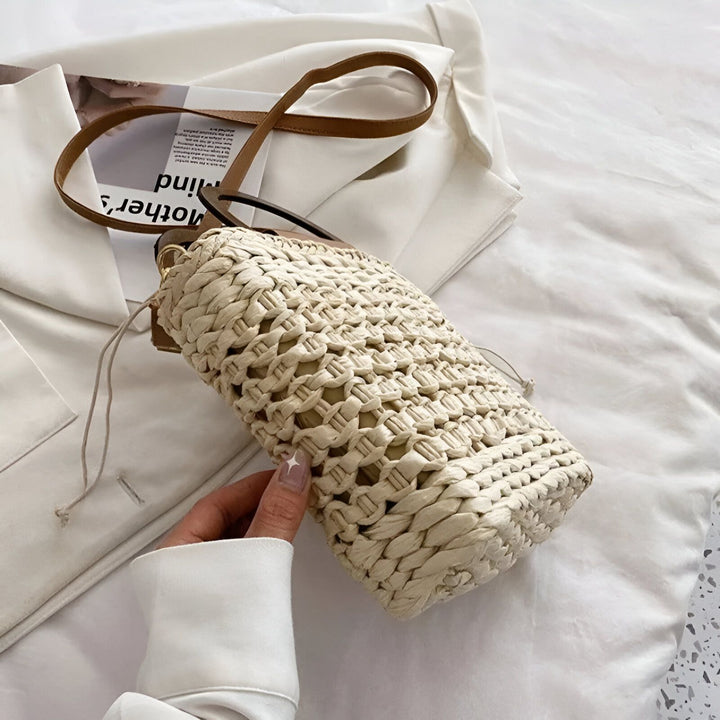Sac à main seau en paille tressée beige avec anse fine en cuir marron sur tissu blanc., 46193946722528,46193946755296