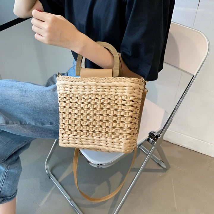 Personne assise tenant un sac cabas en paille avec anses et bandoulière en cuir., 46193946722528,46193946755296