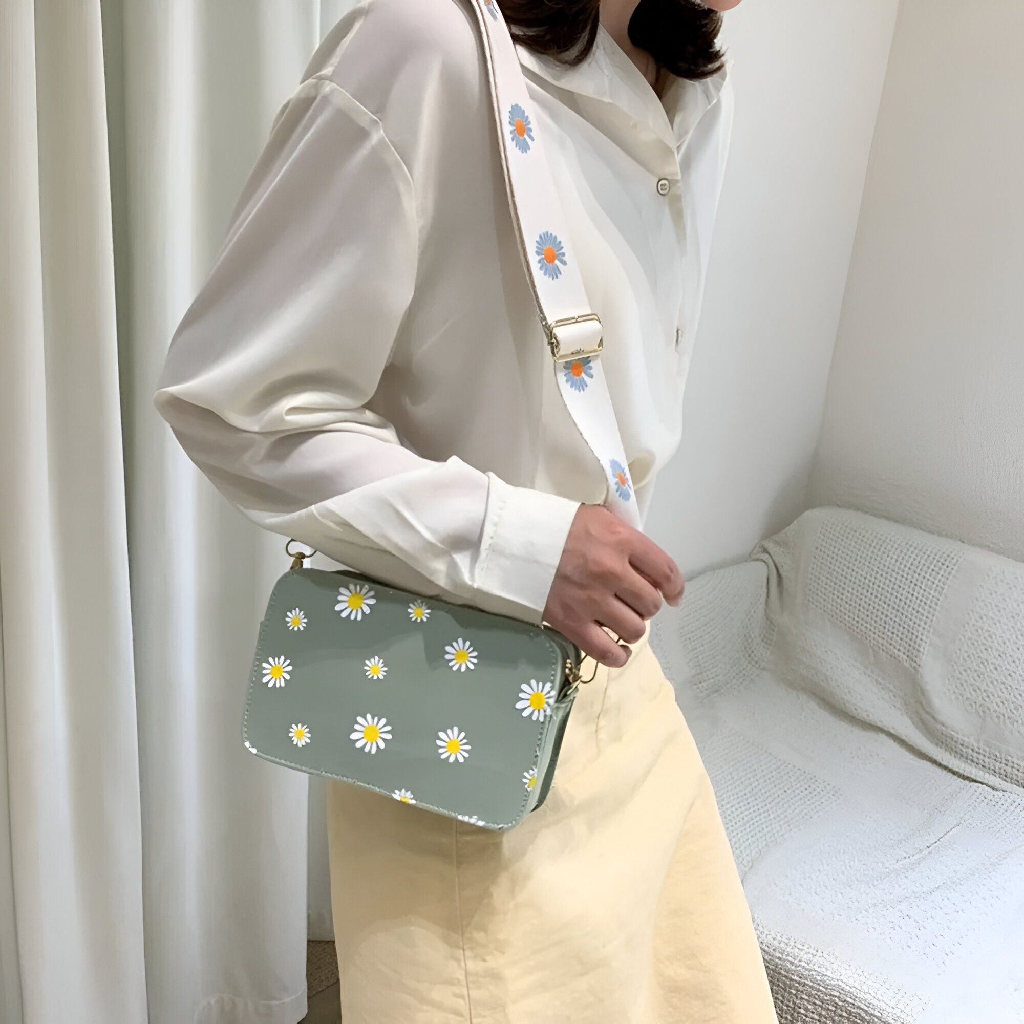 Une femme portant un sac à bandoulière vert avec un motif de marguerites blanches. Le sac a une bandoulière blanche avec un motif de marguerites bleues.