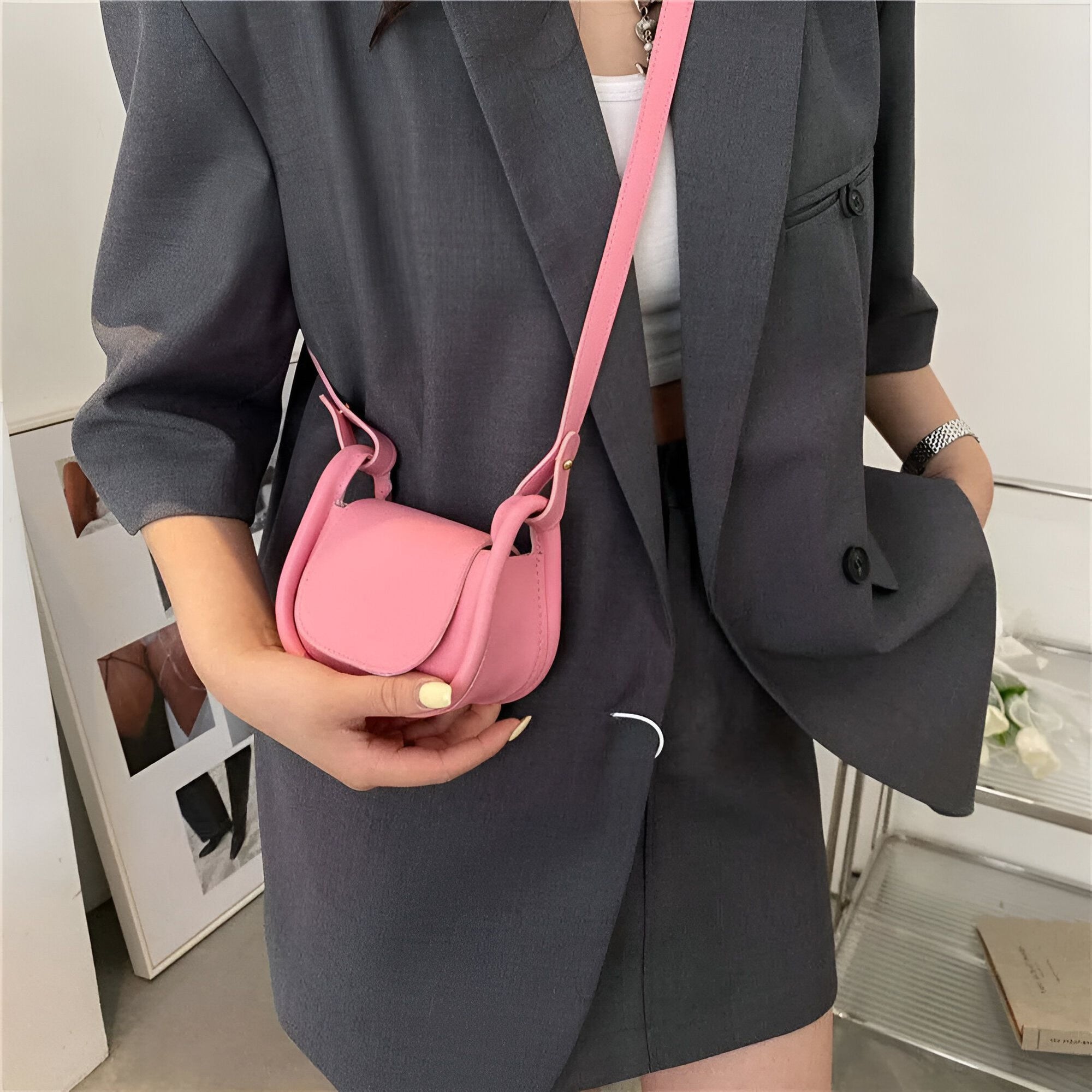 Une femme portant un blazer gris et un petit sac à bandoulière rose.