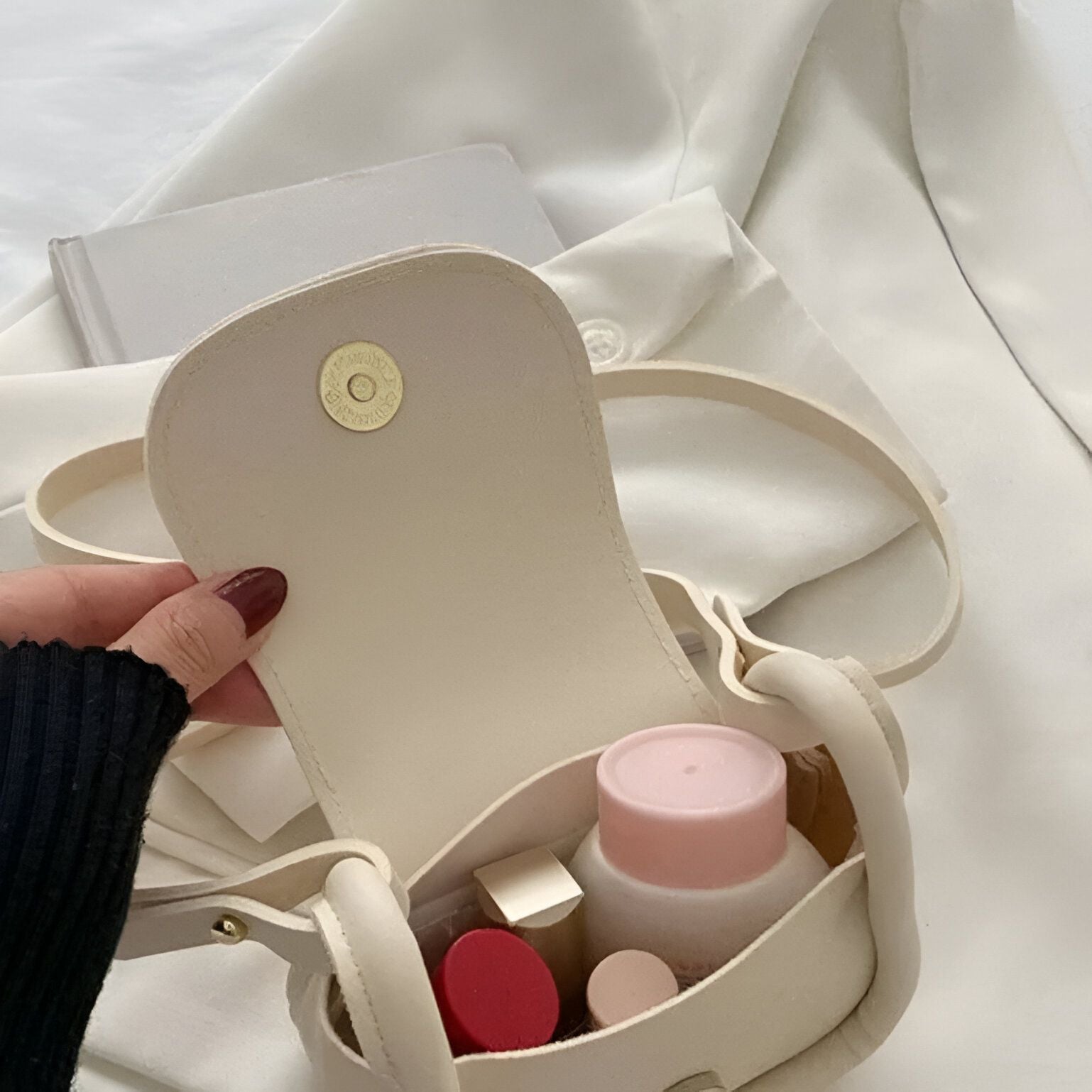 Un petit sac à main beige avec une fermeture à bouton-pression et contenant des produits de beauté.