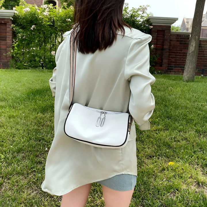 Femme de dos avec veste satinée verte pâle et sac blanc à bandoulière, dans un jardin., 46266441433312,46266441466080,46266441498848