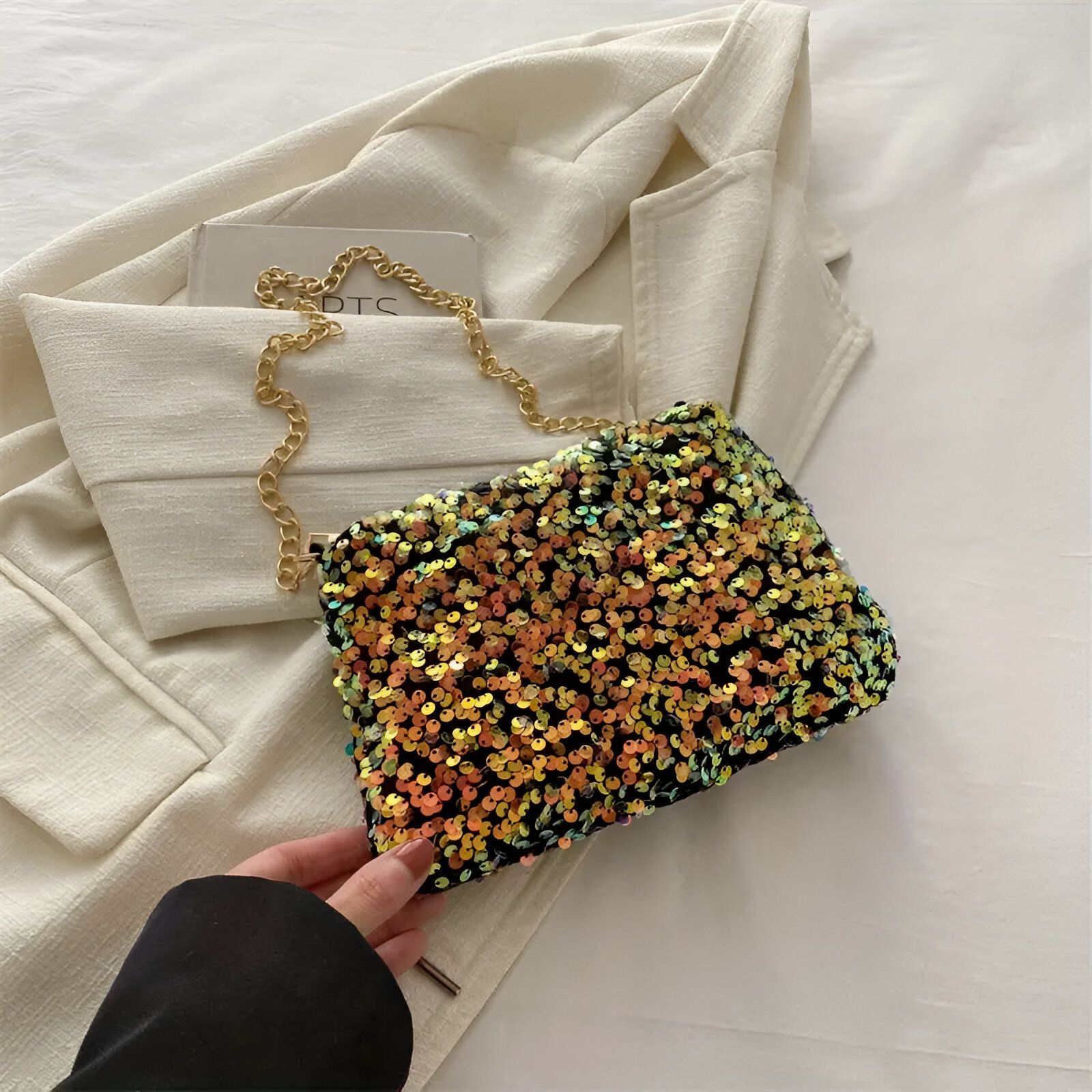 Un petit sac à main noir recouvert de paillettes dorées et argentées.  Il a une chaîne dorée.