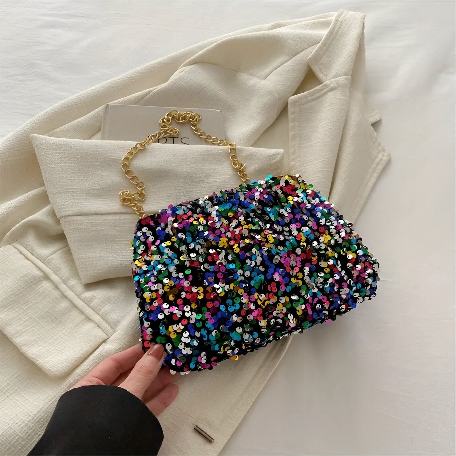 Un petit sac à main noir avec une chaîne dorée et des paillettes multicolores.