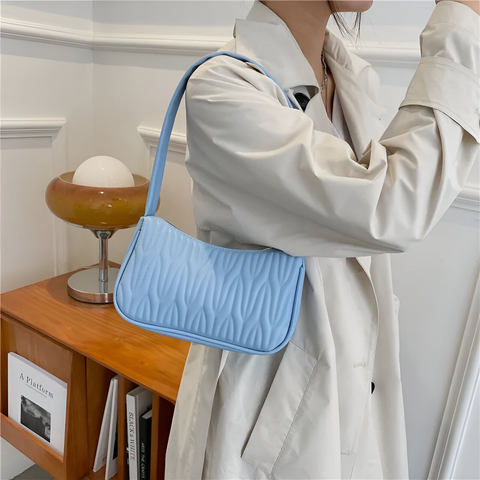 Un sac à main bleu clair matelassé porté par une femme portant un trench beige.