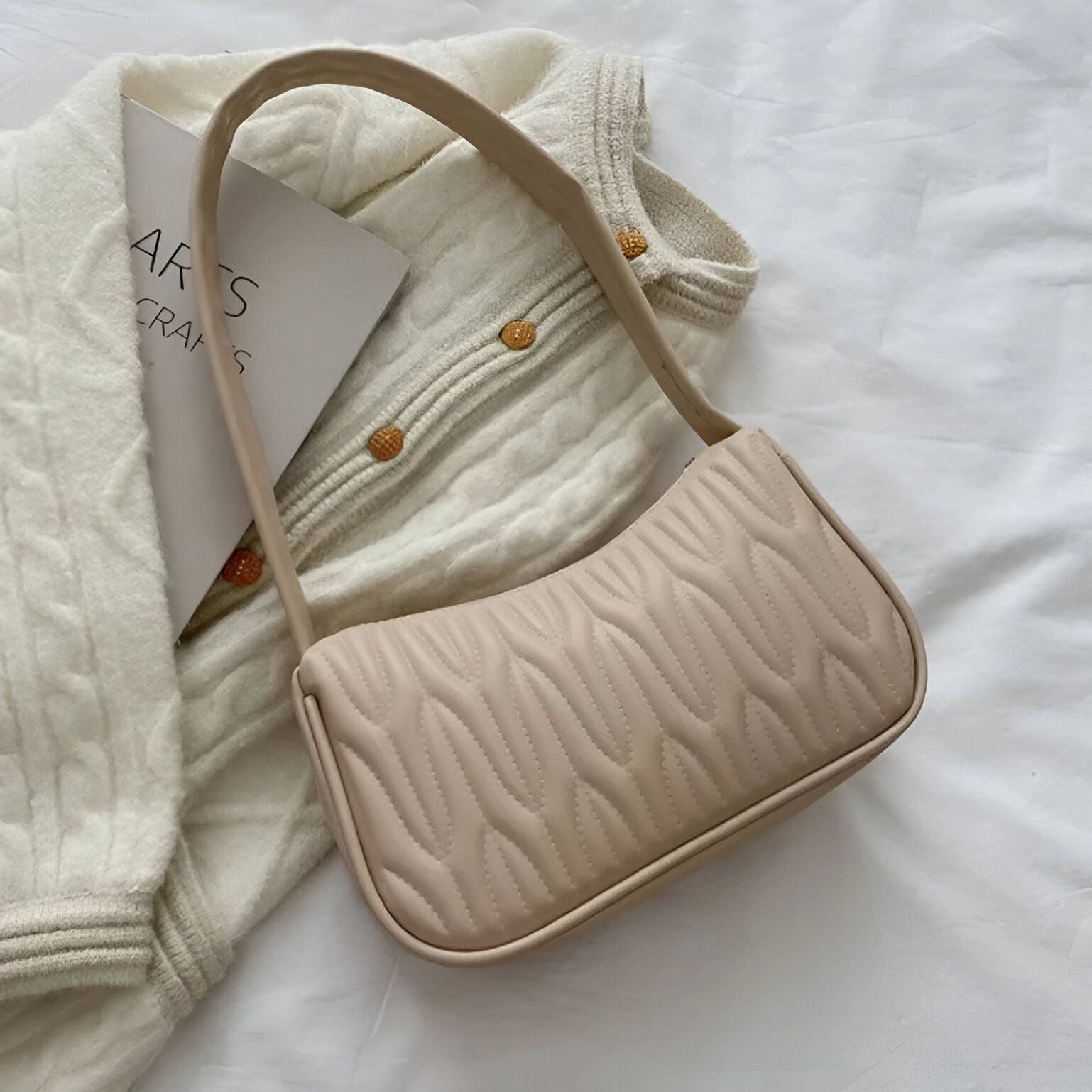 Un sac à main beige matelassé sur un cardigan blanc cassé.