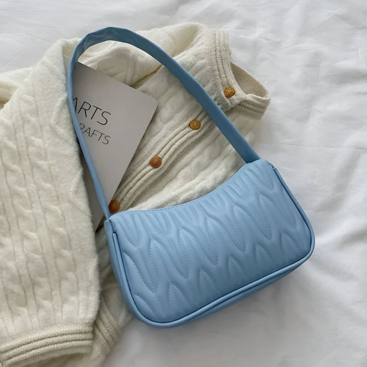 Un petit sac à main bleu sur une veste en tricot blanc cassé.