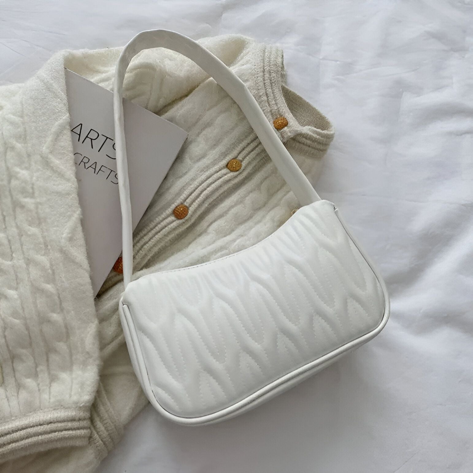 Un sac à main blanc matelassé sur un pull en tricot blanc.