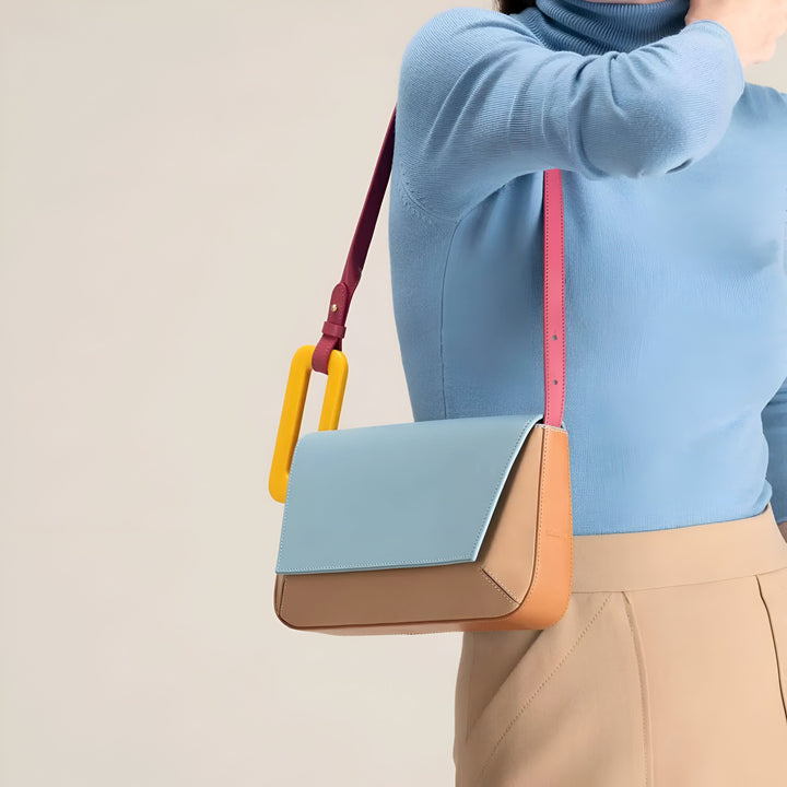 Sac bandoulière structuré bleu clair et beige avec lanière magenta et anneau jaune, porté sur un pull bleu., 46193873715424,46193873748192,46193873780960,46193873813728,46193873846496