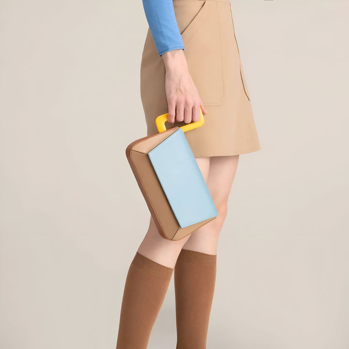 Sac à main bicolore marron et bleu avec poignée jaune, tenu par une femme en jupe beige., 46193873715424,46193873748192,46193873780960,46193873813728,46193873846496