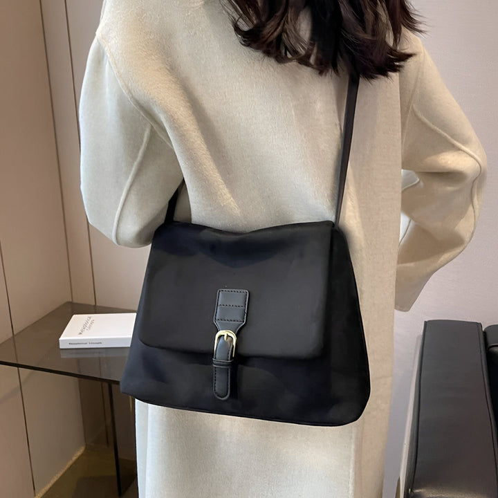 Sac bandoulière noir avec boucle dorée sur une personne portant un manteau clair., 46193887510752,46193887543520