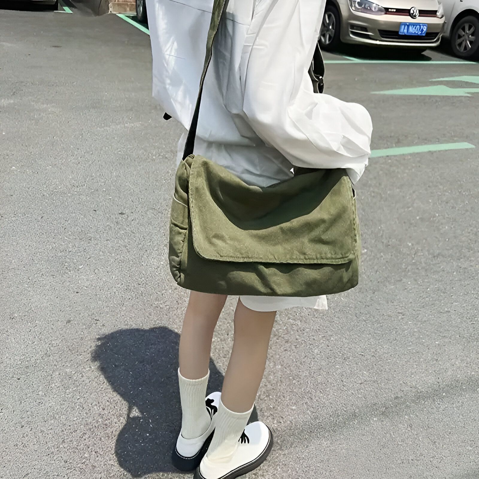 Une femme portant un sac à bandoulière vert sur une chemise blanche et des chaussettes blanches.