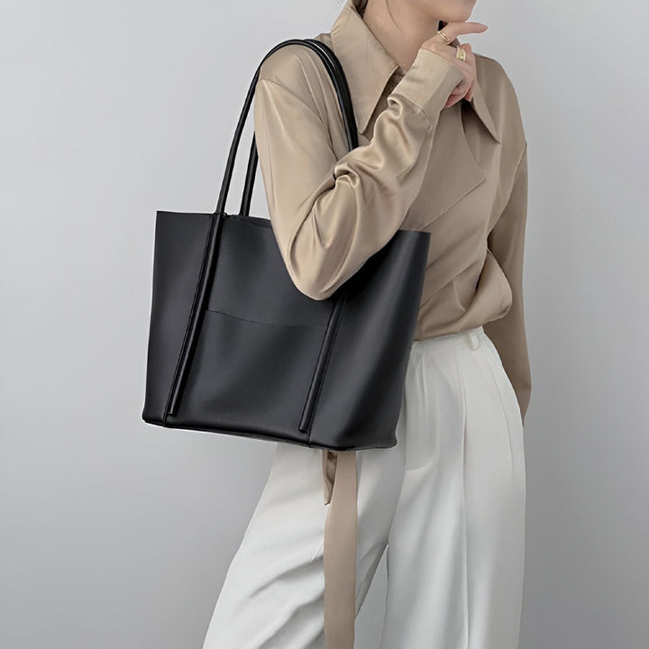 Sac tote noir porté épaule par une femme en chemise beige et pantalon blanc., 46194055643360