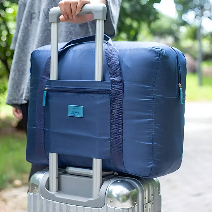 Sac de voyage bleu posé sur la poignée d'une valise à roulettes, tenu par une personne dehors, 46193919852768,46193919885536,46193919918304,46193919951072,46193919983840