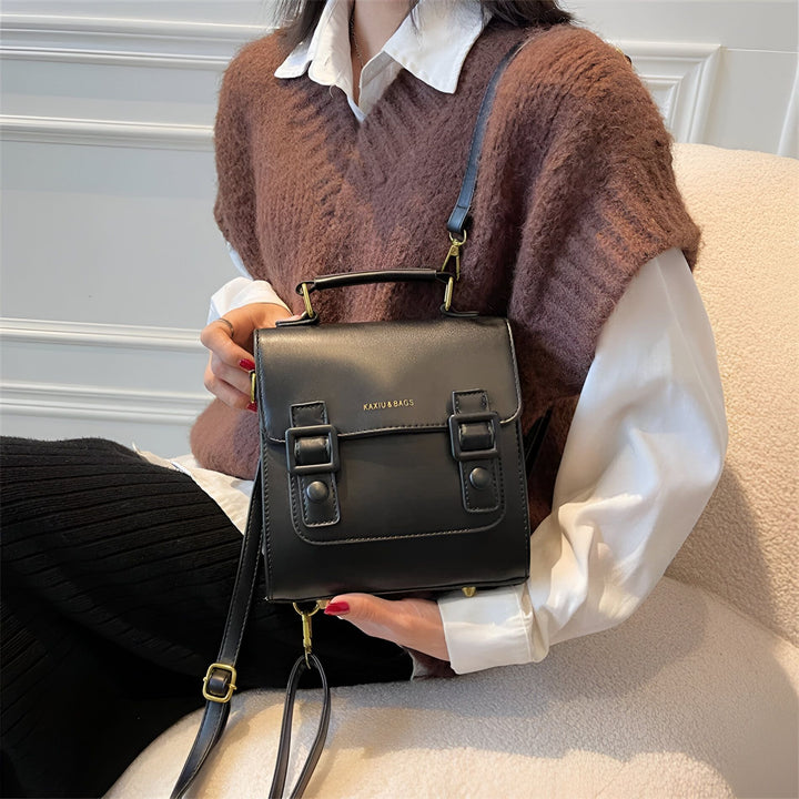 Sac à main noir tenu par une personne, avec sangle épaule et boucles., 46194003312864,46194003345632,46194003378400,46194003411168