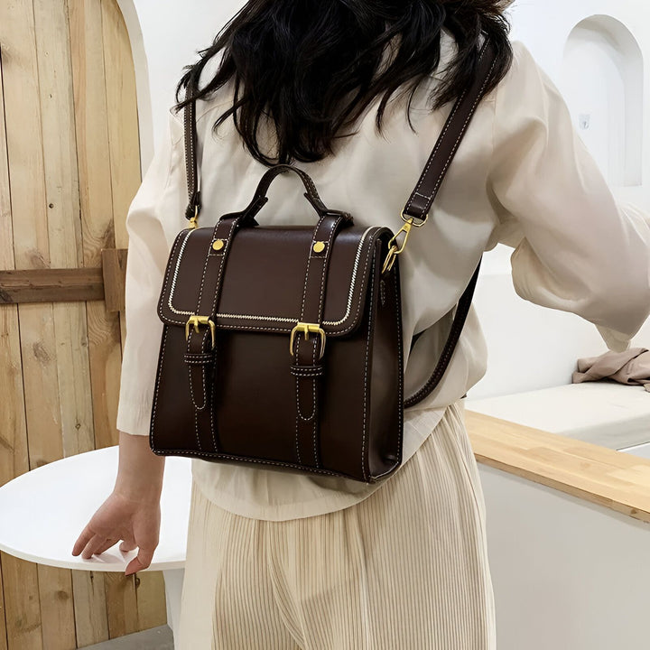 Femme vue de dos portant un sac à dos marron foncé avec boucles dorées., 46193899569376,46193899602144,46193899634912
