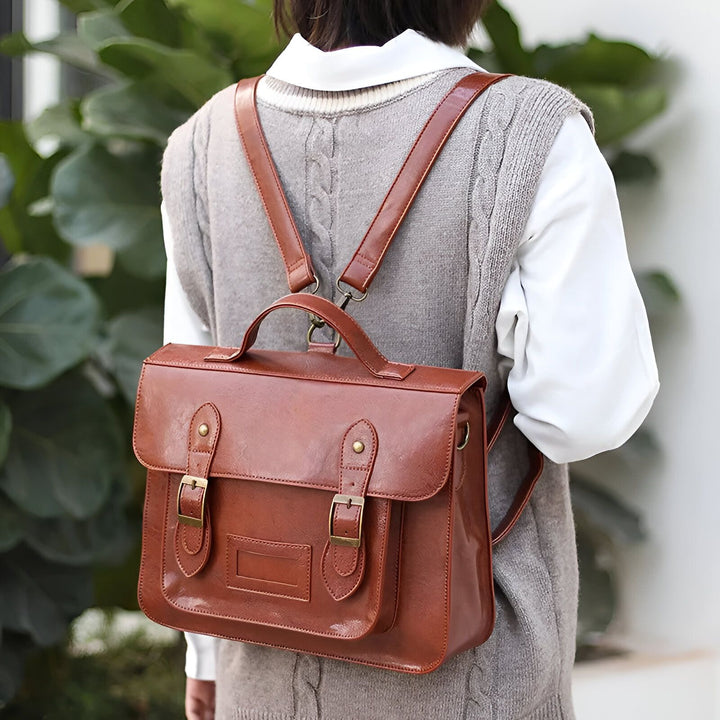 Sac à dos cartable en cuir marron porté sur le dos, avec un gilet gris., 46193905008864,46193905041632
