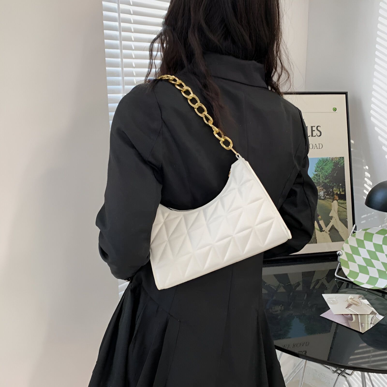 Une femme portant un blazer noir avec un sac à main blanc matelassé et une chaîne dorée.