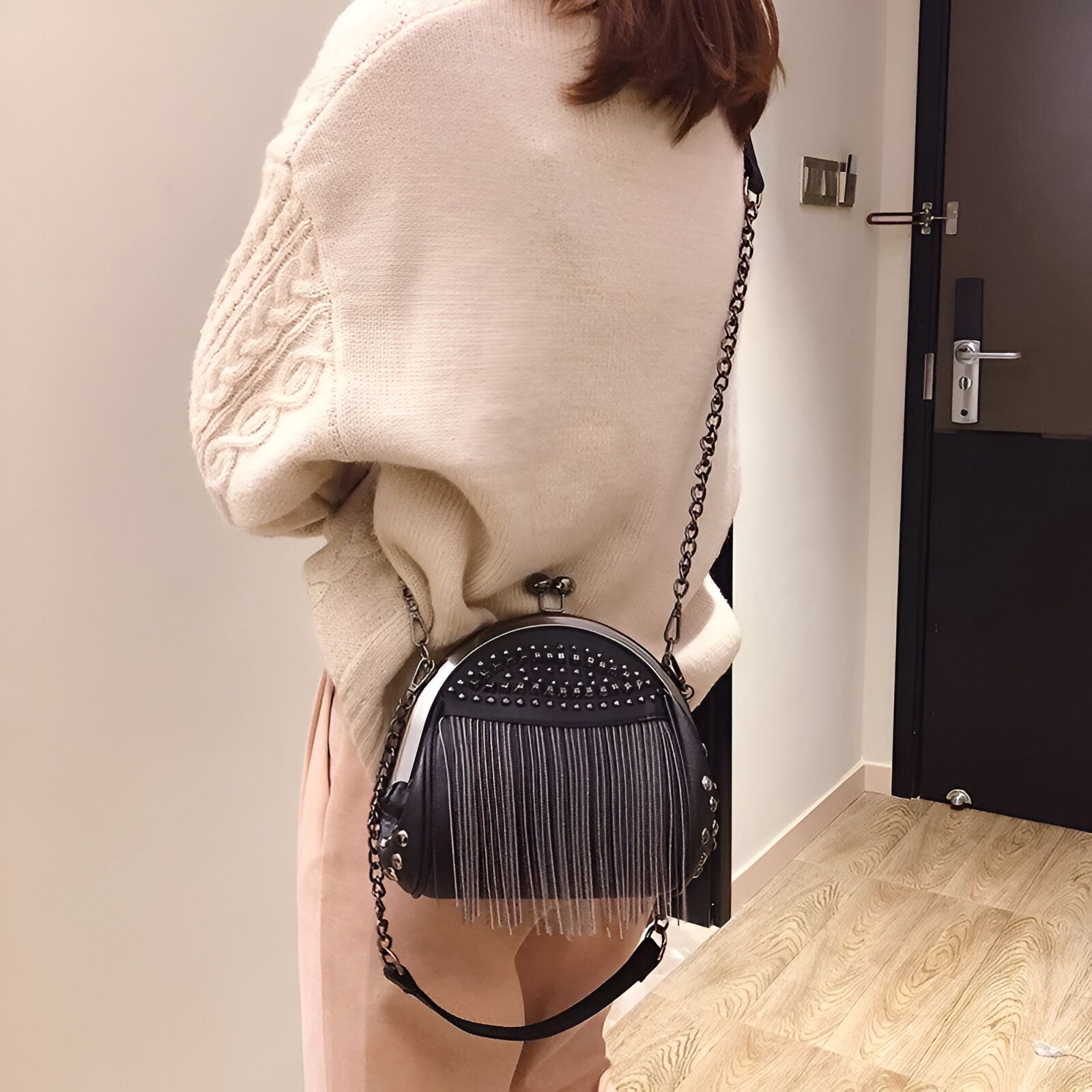 Une femme porte un sac à main noir avec des franges et des clous. Le sac est porté en bandoulière et a une chaîne en métal.