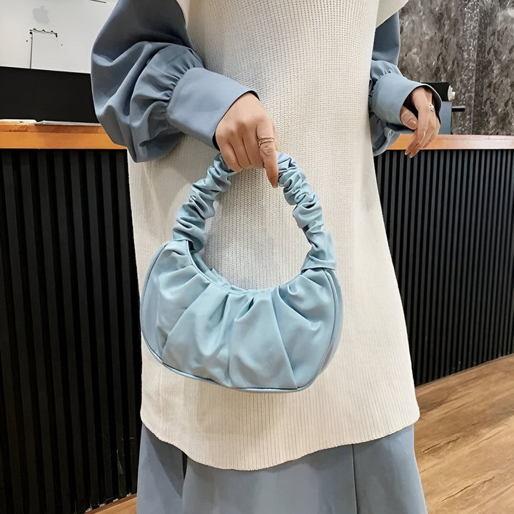 Sac à bandoulière bleu clair froncé tenu par une main., 46193963401440,46193963434208,46193963466976,46193963499744,46193963532512