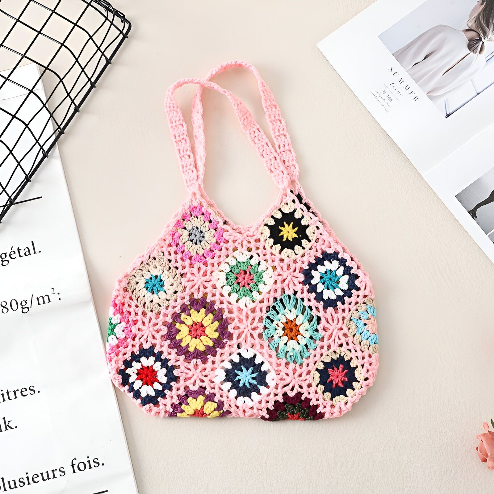 Un sac à main rose en crochet avec des motifs floraux multicolores.