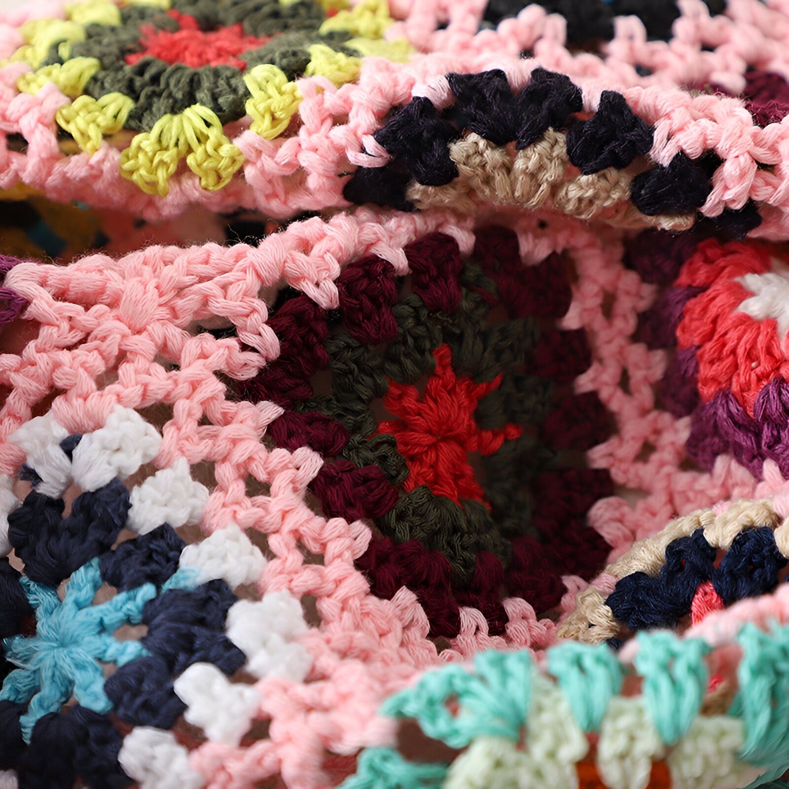 Un tissu crocheté coloré avec des motifs en rose, rouge, vert, bleu, blanc et beige.